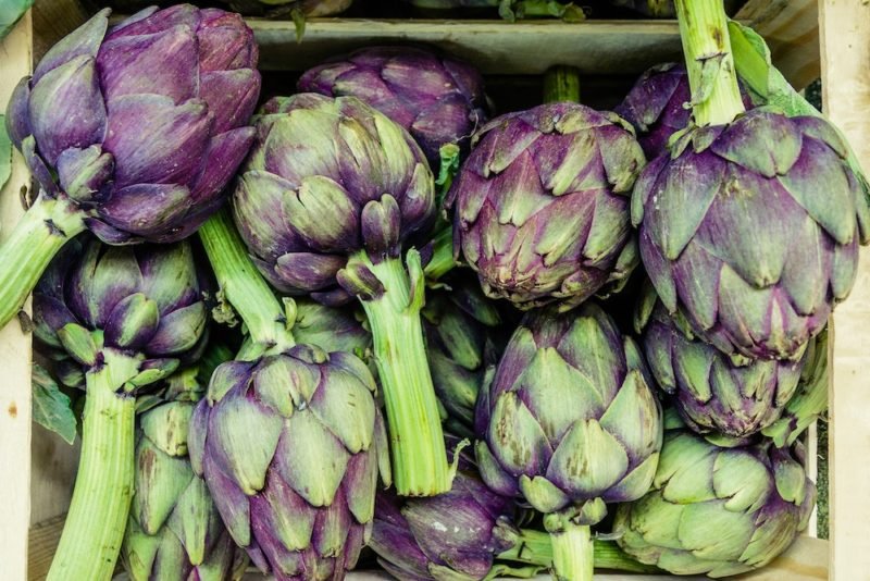 Photo of a wooden crate of green and purple artichokes, which are one source of prebiotic fiber.