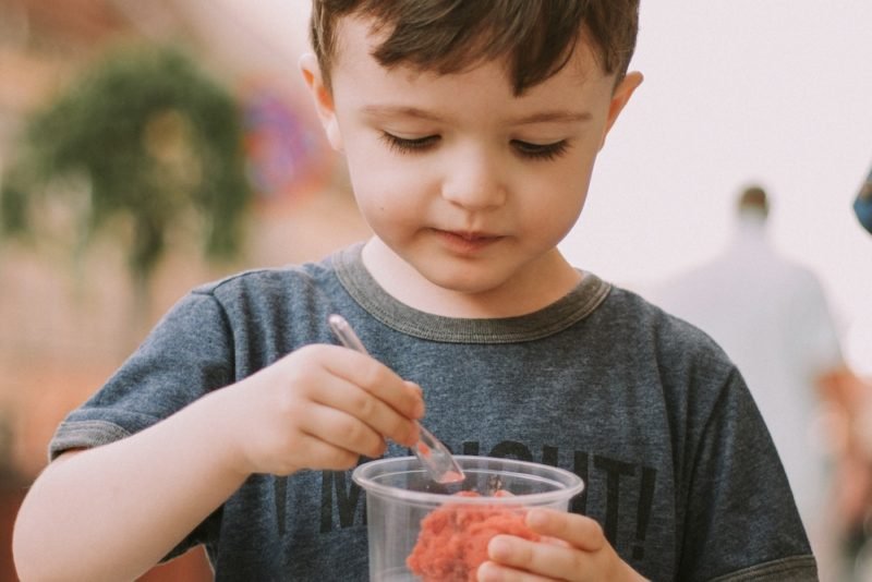 Childhood weight comments might cause the young child in this photos, wearing a heathered gray T-shirt and looking fondly at the pink sorbet in the clear cup he's holding, from enjoying that frozen treat.