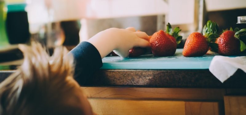 Childhood weight comments might stop this young child from reaching up to pluck a gorgeous red strawberry from the blue cutting board on the kitchen counter, as seen in this photo.