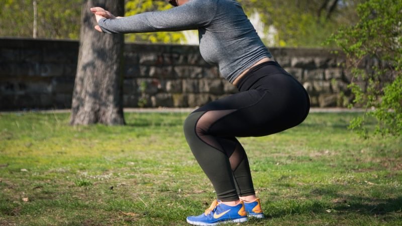 Exercise motivation. Photo of a woman in black leggings, a gray long-sleeved workout top, and blue and orange Nikes doing a squat in a park.