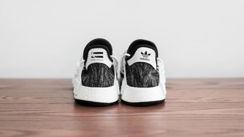 Exercise motivation. Back view of a brand new pair of charcoal and white Adidas sneakers, on a hardwood floor in front of a white wall.