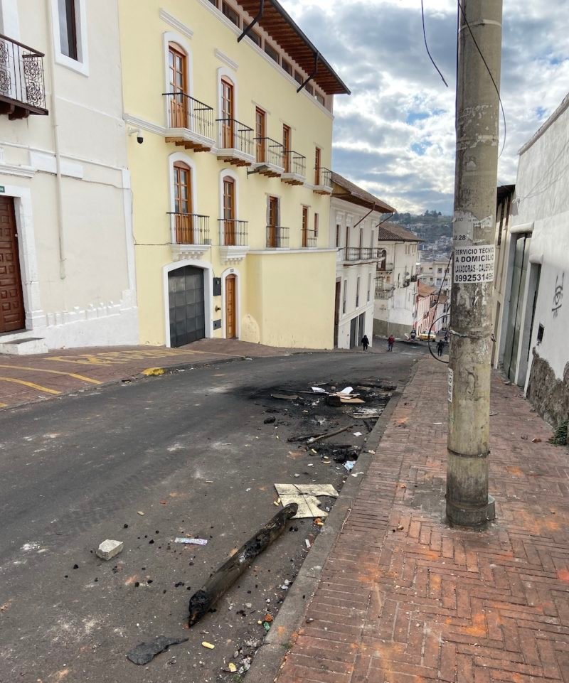 Photo of a street in Quito, Ecuador with remnants of burned wood and debris from the previous night's protests laying in the street.