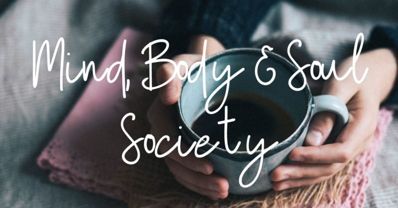 Photo of a woman's hands cupping a blue mug on a pink cloth napkin, with the words "Mind, Body & Soul Society" overlaying the photo.