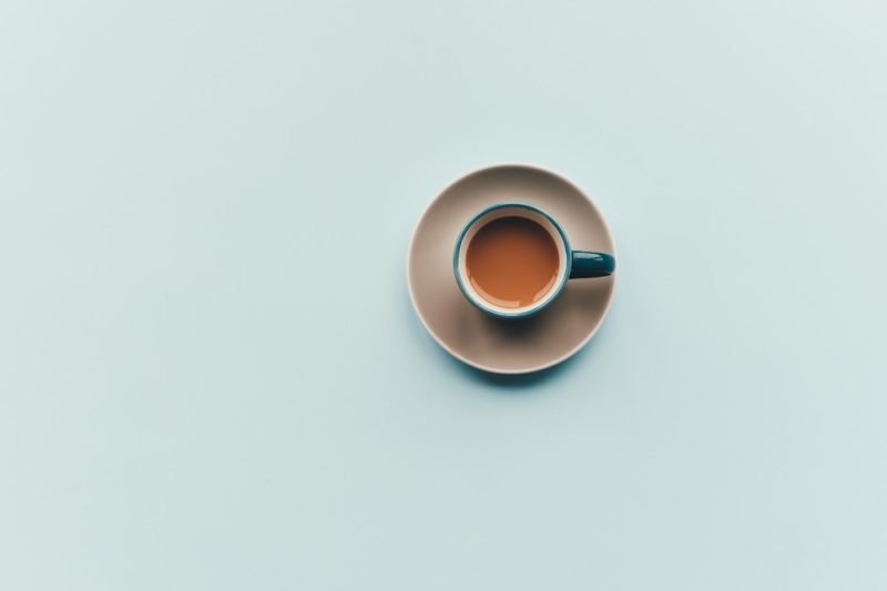 Overhead photo of a brown-and-blue cup and saucer of coffee in the middle of a pale blue background.