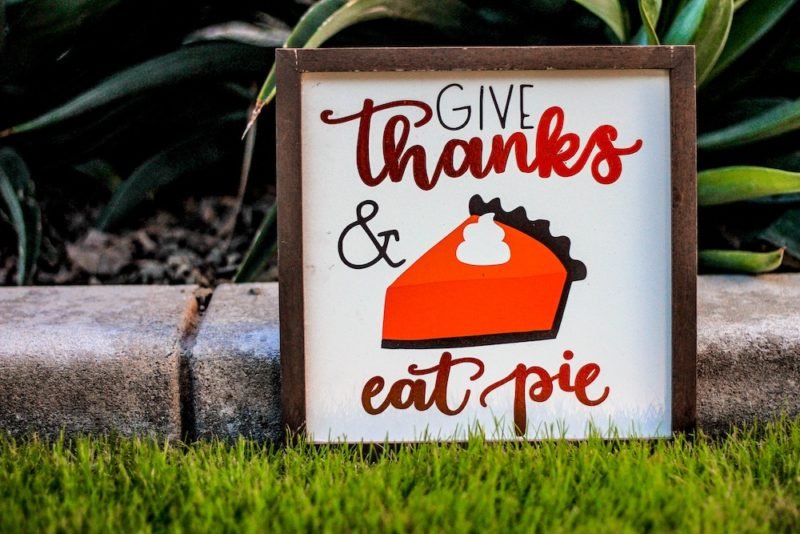 Photo of a sign that says "Give Thanks and eat pie," with a drawing of a red slice of pie with dark brown crust. Mindfulness during the holidays can increase our happiness.