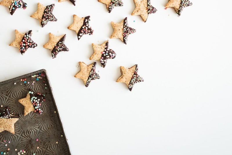 Mindful Eating Holidays: When you approach the holidays mindfully, you can enjoy holiday favorites in a balanced way. Top view photo of a corner of an antique baking sheet, surrounded by a scattering of star-shaped sugar cookies half-dipped in chocolate and sprinkles.