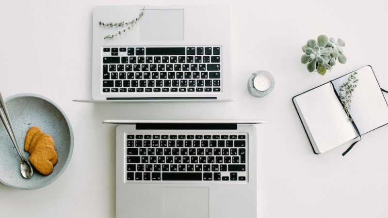 Nutrition myth busting. Overhead photo of two open laptops, back-to-back, along with a rustic blue plate with some heart-shaped cookies and a long handled-spoon, and an open hard-bound notebook.