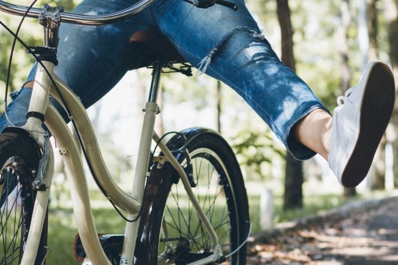 Enjoyable exercise could be riding your bike like you're a kid again, as in this photo of a women in ripped jeans and white sneakers, coasting on a bike with her feet outstretched, on a tree-lined road.