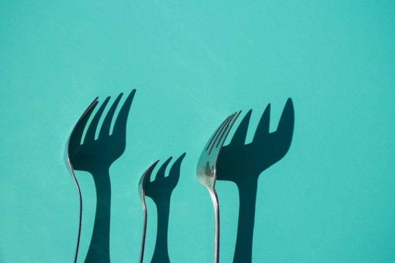 Part of weight bias in the media is perpetuating the idea that obesity and climate change can both be solved with our forks. Image of three forks with large shadows against a turquoise background.