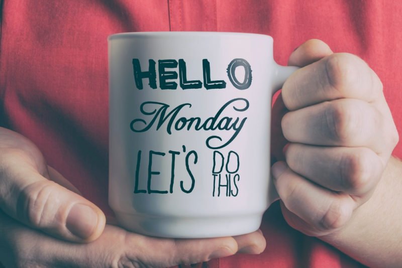 On of the pitfalls of motivation is that you can get stuck in a pattern of doing, and never slowing down. Close-up photo of a woman in a red shirt holding a white mug reading "Hello Monday, let's do this" in black script.