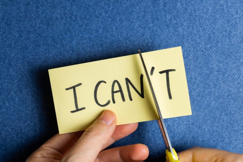 On of the pitfalls of motivation is thinking that you have to have some in order to take action. Close-up photo of a yellow stickie note with "I can't" written on it in black marker, being held by someone who is cutting off the end of the word so it will read, "I can."