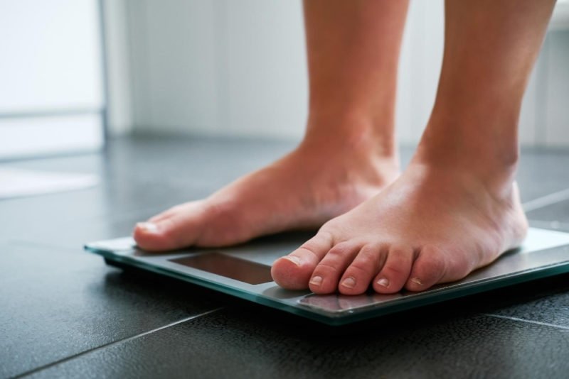 A non-diet approach does not include intentionally pursuing weight loss. Photo of a woman's bare feet and ankles as she stands on a digital bathroom scale.