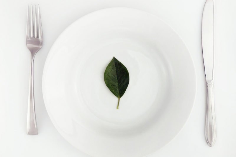 Elimination diets often restrict too many foods. Photo of white plate with a single leaf on it, on a white background