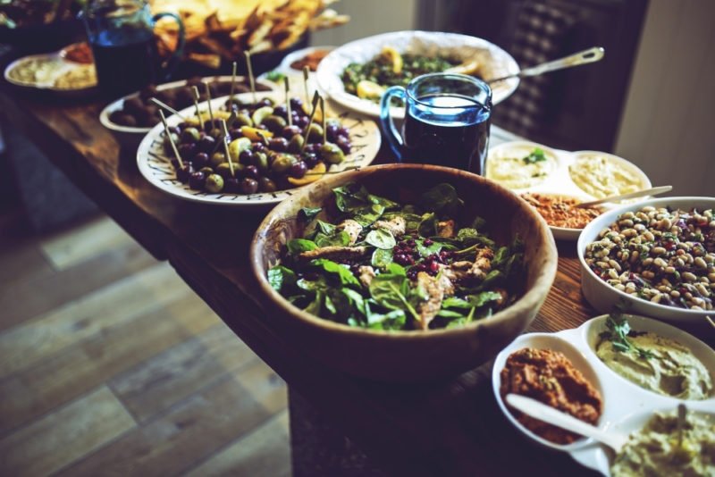 When you make peace with food, this increases the variety of foods in your diet, which improves both nutrition and pleasure. Photo of a buffet table with Mediterranean-type foods, including olives, a bean salad, hummus and tapenades, bread, and a spinach salad with chicken and pomegranate arils