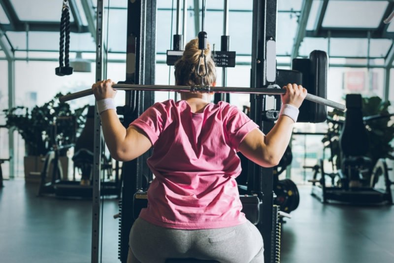 Woman plus size in gym doing exercises with training apparatus