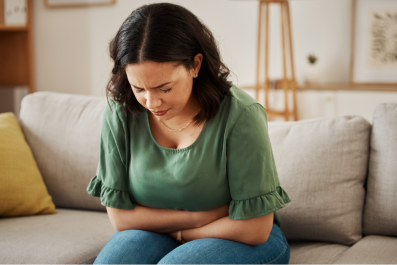 Woman sitting on couch with her arms wrapped around her stomach because of IBS symptoms.