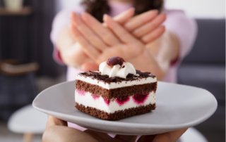 Close up of a piece of birthday cake in front of a woman's hands held up in a "no" gesture