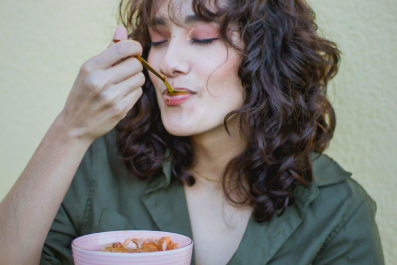 A young woman enjoys a spoonful of cereal with her eyes closed as she notices how the food satisfies her and makes her feel.