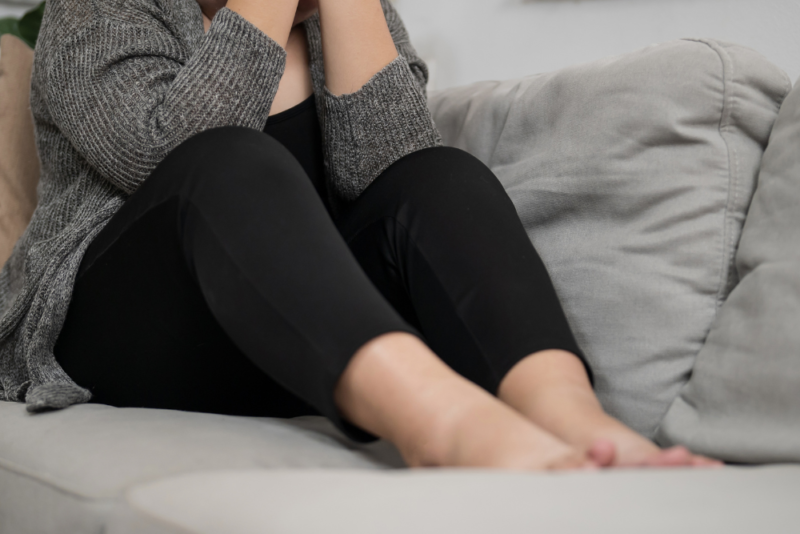 Young plus size woman in black leggings and a gray cardigan sitting with her face in her hands because of body dissatisfaction related to internalized weight bias.