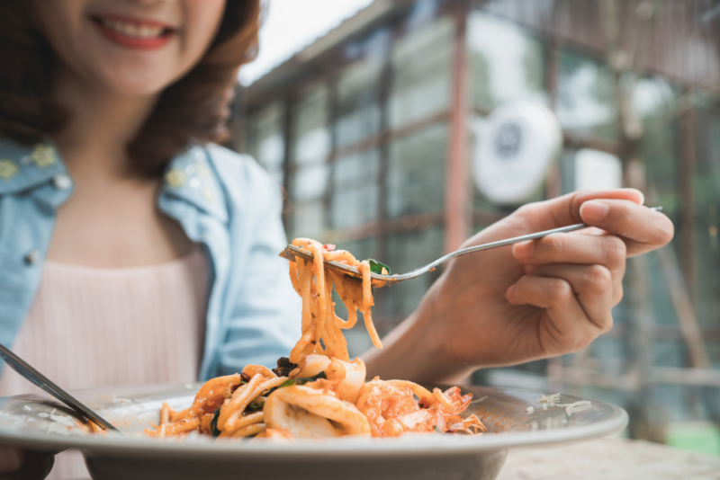 A woman satisfying her physical hunger with a pasta dish at a restaurant.