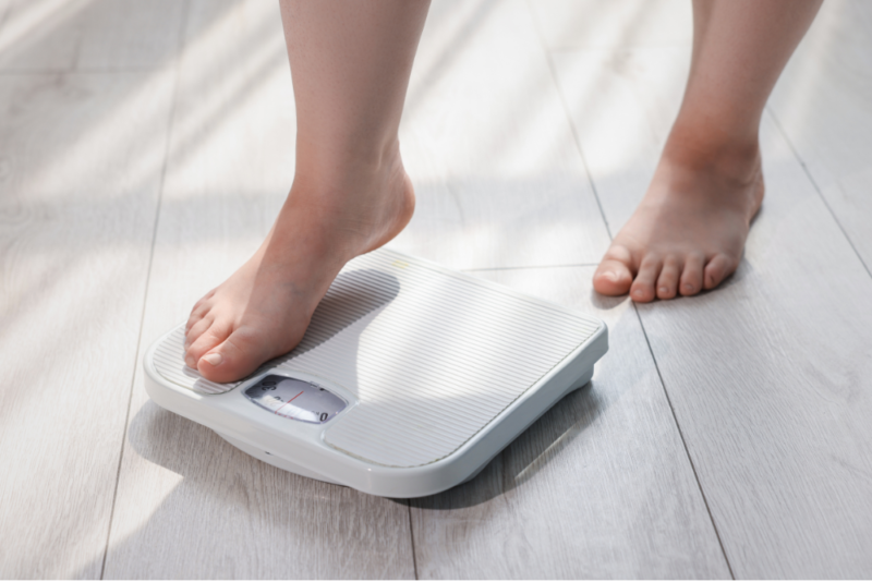 Woman's legs from the shin down, with one foot stepping on a bathroom scale.